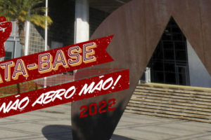 A imagem mostra o prédio da Assembleia Legislativa de Minas Gerais com uma escultura do artista Amilcar de Castro em primeiro plano. A escultura é um semi circulo em metal marrom com um um corte central triangular. Ao fundo do prédio o céu é azul.