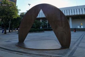 fachada da Assembleia Legislativa de Minas Gerais com destaque para o monumento que consiste em um triângulo vazado em um círculo de bronze.