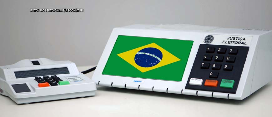 fundo branco e em destaque urna eletrônica eleitoral com a bandeira do Brasil na tela.