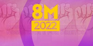 Em um fundo de tons roxos, punhos femininos erguidos para o alto como símbolo de luta. No centro o texto "8M 2022" em amarelo