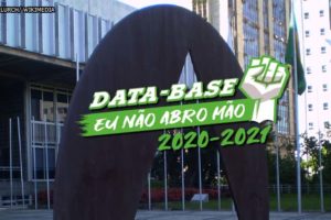 Fachada da Assembleia Legislativa de Minas Gerais. Sobre a foto, há uma ilustração de um punho cerrado para o alto nas cores branco e verde com o conteúdo textual escrito na cor branca: Data-Base, eu não abro mão! 2020-2021.