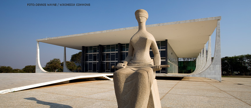 Foto da escultura "A Justiça", localizada em frente ao prédio do Supremo Tribunal Federal, na Praça dos Três Poderes, em Brasília. O monumento representa uma mulher, sentada e vendada, segurando uma espada, um dos símbolos mais usados para caracterizar as deusas greco-romanas das leis e da justiça. Conteúdo textual: Nota. Fenajud repudia ataque de Roberto Jefferson a policiais federais e afronta à decisão judicial.