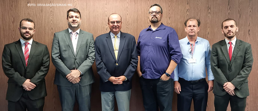 Em pé em frente uma parede de madeira estão (da esquerda para a direita): Felipe Rodrigues, diretor de Finanças do SINJUS-MG, Eduardo Couto, presidente do SERJUSMIG, Desembargador José Arthur Filho, presidente do TJMG, Eduardo Rocha, diretor-geral do SINDOJUS/MG, Rui Viana, 1º vice-presidente do SERJUSMIG e Alexandre Pires, coordenador geral do SINJUS-MG.