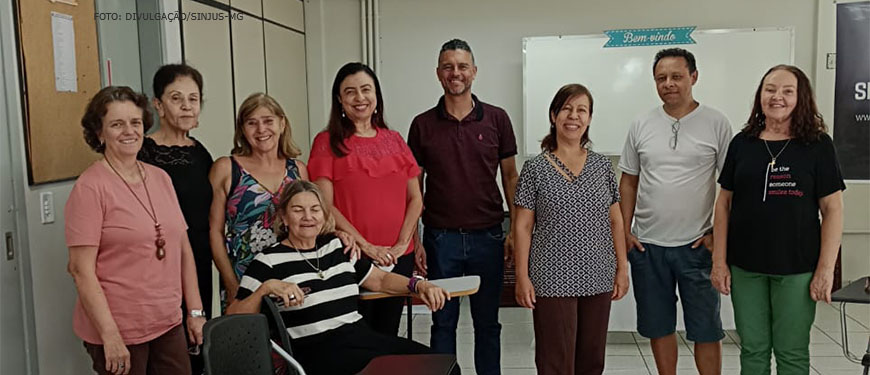 Foto do grupo que esteve presente no encontro do NAP, estão na foto, a partir da esquerda: uma mulher de pele clara, cabelos curtos e castanhos, vestindo uma blusa cor de rosa; uma mulher de pele clara e cabelos bem curtos, vestindo uma blusa preta; mulher de pele clara, loira, com uma blusa de alças finas bem colorida; uma mulher de cabelos médios e pele clara, vestindo uma blusa de cor vermelha; um homem alto, de pele clara com cabelos curtos e pouco grisalhos, vestindo uma blusa na cor vinho; uma mulher de pele clara e cabelos médios presos para trás, vestindo uma blusa nas cores preto e branco; um homem de pele parda e cabelos castanhos, vestindo uma blusa branca com um óculos de grau pendurado na gola; uma mulher de cabelos médios e castanhos, pele clara, vestindo uma blusa na cor preta. À frente de todos temos, sentada, uma mulher de pele clara, cabelos curtos e loiros, vestindo uma blusa listrada nas cores preto e branco. Conteúdo textual: APOSENTADOS E PENSIONISTAS. QUIZ DO MÊS DO SERVIDOR É ATRAÇÃO DO ENCONTRO DO NAP