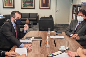 A imagem contém quatro pessoas reunidas em uma mesa de madeira, sendo que, sentados de um lado os dirigentes do SINJUS Alexandre Pires e Felipe Rodrigues, e do outro 1º vice-presidente do TJMG, desembargador Alberto Vilas Boas, e com a juíza auxiliar da 1ª Vice-Presidência, Mônica Silveira Vieira. No fundo da imagem existe uma parede branca com cinco quadros emoldurados em madeira um conjunto de sofás na cor preta. 